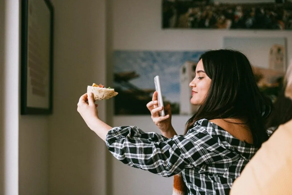 Content creator taking a selfie with her phone while holding food